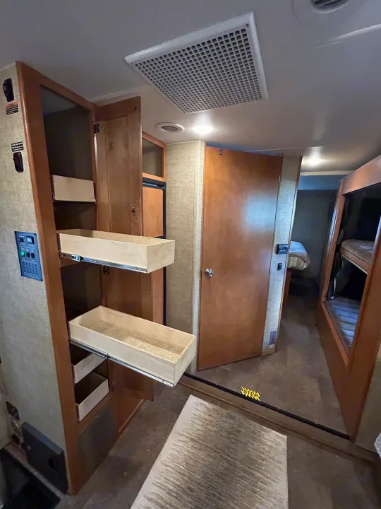 RV rental interior showcasing smart storage: pull-out pantry drawers, a control panel, bunk beds, and bedroom access.. Winnebago Minnie Winnie 2017