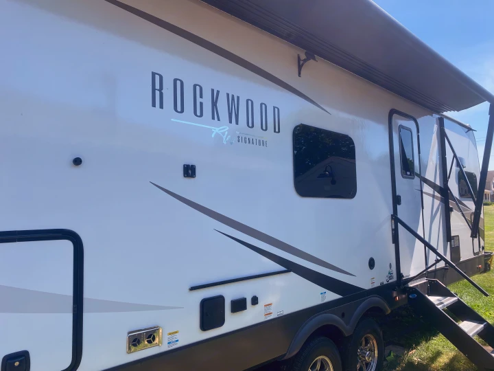 This white Rockwood Signature RV, perfect for an rv rental, stands with its side awning extended and steps deployed.. Forest River Rockwood Signature 2024