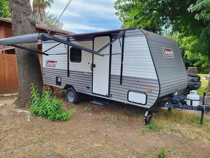Grey and white Coleman travel trailer with extended awning, parked outdoors. Ideal for your next RV rental adventure.. Dutchmen Coleman Lantern LT 2023