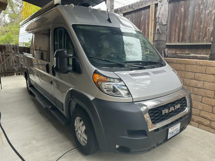 Grey camper van, an excellent rv rental option, parked on concrete beside a wooden fence.. Thor Sequnce 2023