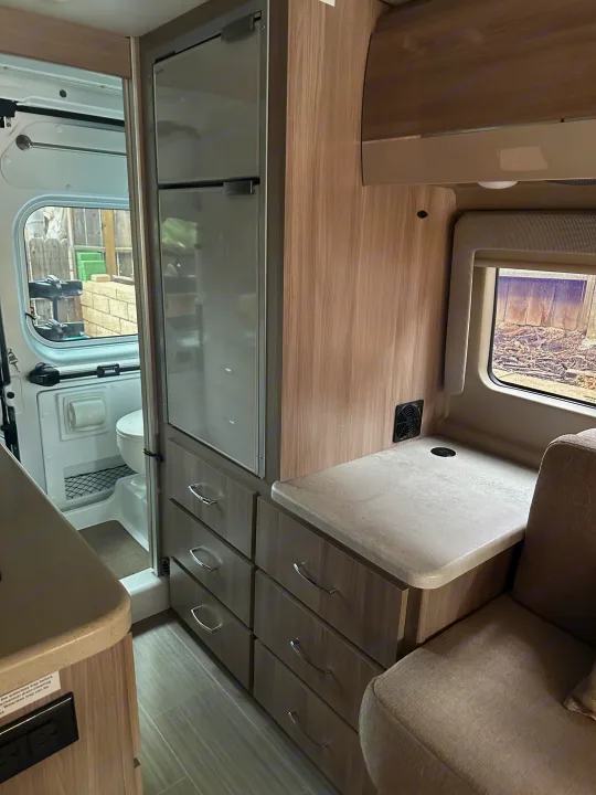 Inside an RV rental: modern compact interior with a refrigerator, multiple drawers, countertop, and a peek into the wet bath.. Thor Sequnce 2023