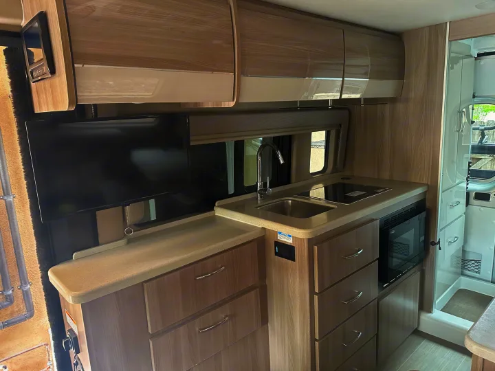 Modern RV rental interior: kitchen with sink, cooktop, microwave, and TV, alongside a shower unit.. Thor Sequnce 2023