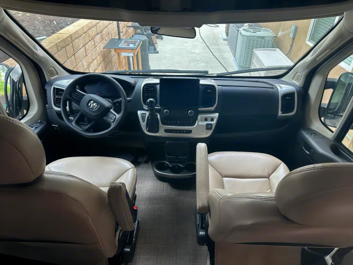 Inside this **rv rental**: beige leather driver and passenger seats, a sleek dashboard with screen, and wide front views.. Thor Sequnce 2023