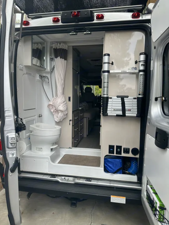 Explore this rv rental's interior. A camper van's rear shows a wet bath (toilet, shower) & storage with a Thule ladder.. Thor Sequnce 2023