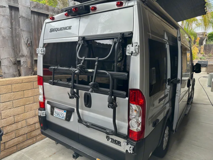 Rear of a silver Thor Sequence camper van with a Thule bike rack, perfect for your next RV rental trip. Doors ajar.. Thor Sequnce 2023