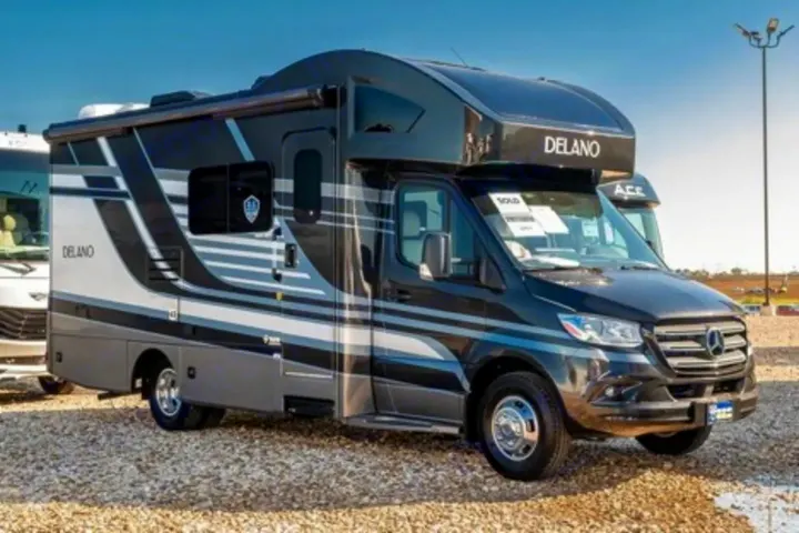 Modern Delano RV rental. This dark grey & white Mercedes-Benz Class C motorhome is parked on a gravel lot under a clear sky.. Thor Motor Coach Delano 2022