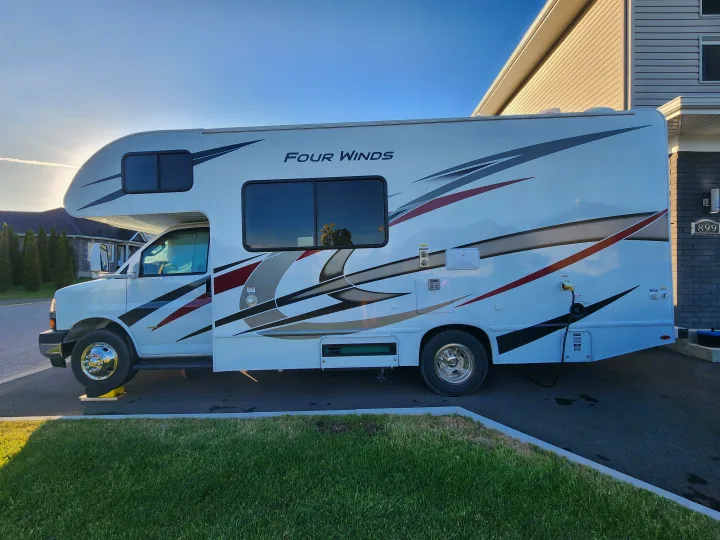 White Four Winds Class C motorhome, an RV rental, parked on a driveway with leveling blocks beside a house.. Thor Four Winds 2024