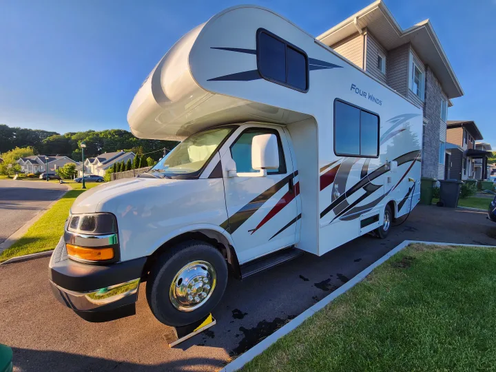 Four Winds motorhome, an RV rental, leveled on a driveway in a residential area on a sunny day.. Thor Four Winds 2024