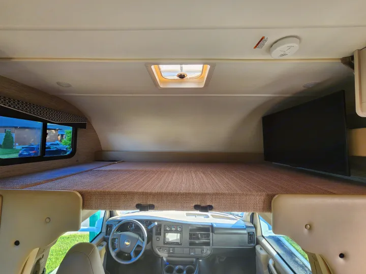 RV rental: Interior view of the cab-over bunk with a bed, TV, and skylight, overlooking the dashboard.. Thor Four Winds 2024