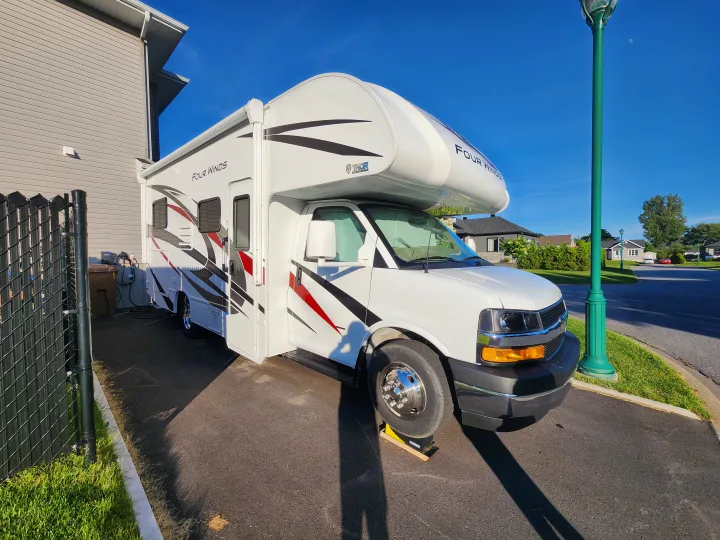 White Thor Four Winds RV rental parked on a paved driveway with power hookups. Bright outdoor scene under clear blue sky.. Thor Four Winds 2024