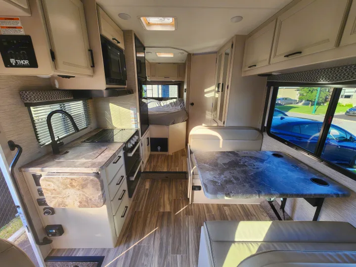 Bright rv rental interior, showcasing the kitchen, dinette with table, and rear bed area.. Thor Four Winds 2024