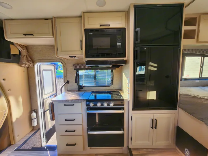 Modern RV rental interior: kitchen with microwave, stove, fridge, and bed area visible. Perfect for a road trip.. Thor Four Winds 2024