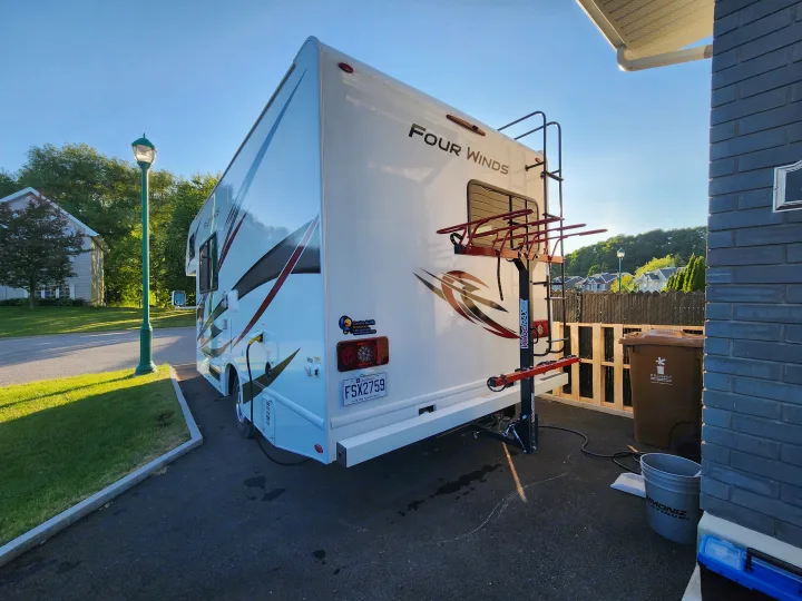 This large white RV rental, featuring a rear bike rack, is parked outside a home, set for a new journey.. Thor Four Winds 2024