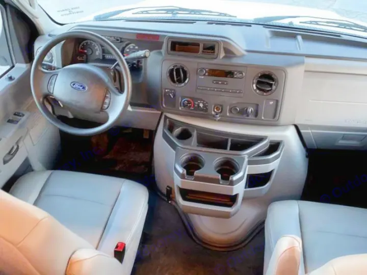 Inside this RV rental's front cabin: driver's seat, Ford steering, dashboard, and central console with cup holders visible.. Tiffin Motorhomes Wayfarer 2021