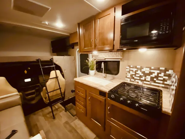 Spacious RV rental interior with full kitchen: microwave, stovetop, sink, and ample storage. Cozy home on wheels!. Winnebago 25J 2019