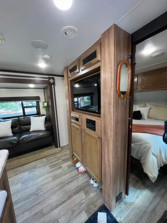 Bright RV rental: living space with dark sofa, wood-look flooring, entertainment center, and master bedroom visible.. Jayco Jay Feather 2019