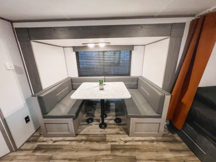 Spacious and modern dinette in an RV rental, featuring a U-shaped booth, marble table, and wood floors for comfortable dining.. Dutchmen Lantern LT BB19 2024