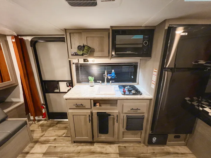 Compact RV rental kitchen interior featuring a sink, two-burner stove, microwave, and refrigerator.. Dutchmen Lantern LT BB19 2024