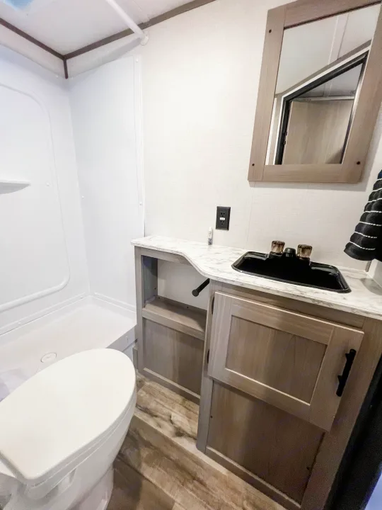 Modern **RV rental** bathroom interior featuring a white shower, toilet, and stylish vanity with black sink.. Dutchmen Lantern LT BB19 2024