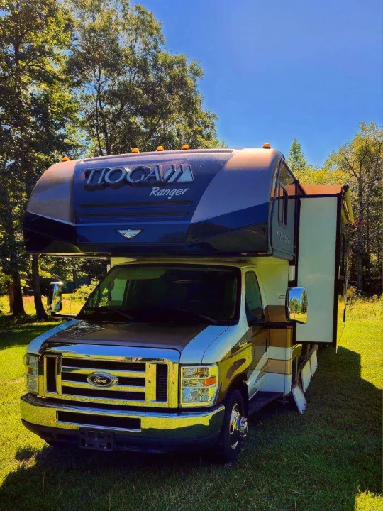 Explore the open road with this Tioga Ranger Class C rv rental. A blue and tan motorhome with a slide-out, parked on sunny grass.. Tioga Ranger 2013