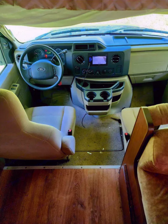 Step into this RV rental! Driver's cockpit view shows the dashboard, steering wheel, front seats, and central console with cup holders.. Tioga Ranger 2013