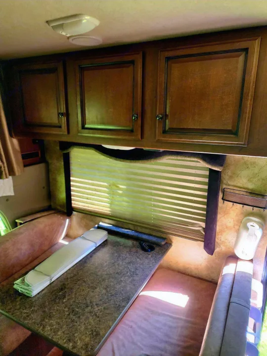 RV rental dinette area featuring overhead wooden cabinets, sunlit window with blinds, and comfy seating.. Tioga Ranger 2013