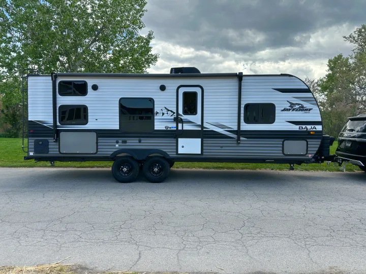 White & grey Jayco Baja travel trailer (RV), perfect for your next rv rental adventure. Parked on asphalt, hitched to SUV.. Jayco Jay Flight SLX Baja Edition 2023