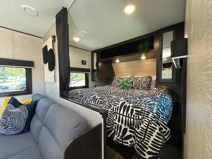 This RV rental offers a modern interior, showcasing a comfy bedroom with bold black & white bedding and a cozy sofa area.. Jayco Jay Flight SLX Baja Edition 2023