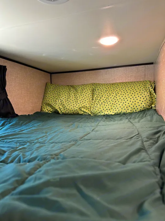 Cozy RV rental bunk bed with dark green bedding and polka dot pillows, featuring an overhead light in a compact space.. Jayco Jay Flight SLX Baja Edition 2023