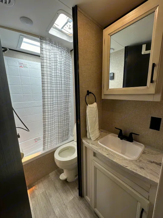 Inside an RV rental: a compact bathroom with shower/tub, toilet, sink, and mirror medicine cabinet.. Jayco Jay Flight SLX Baja Edition 2023