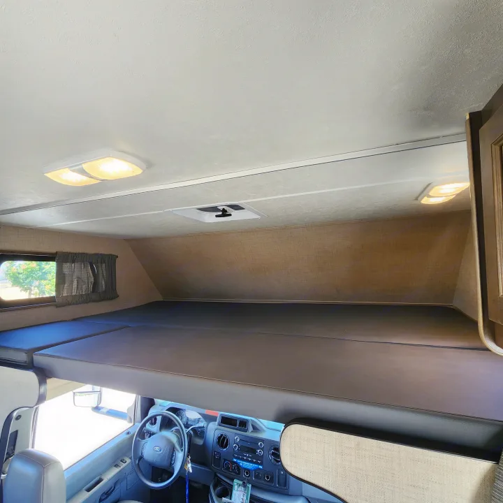 Inside this RV rental: a cozy cab-over bunk bed and the cockpit area with dashboard and steering wheel.. Thor Majestic 2019