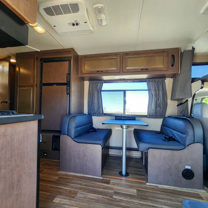 Cozy RV rental interior showing a dinette with bench seats, kitchen, fridge, and overhead storage.. Thor Majestic 2019