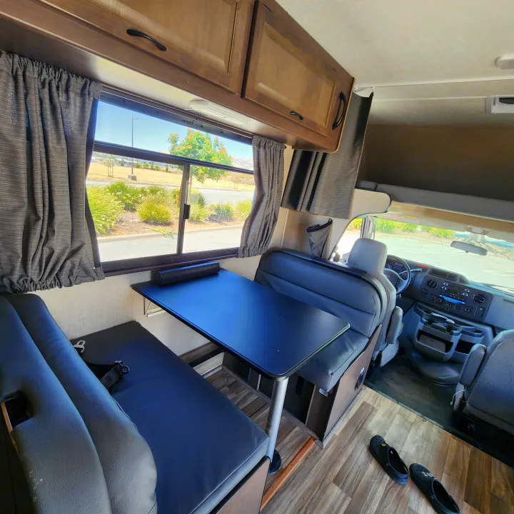 This RV rental features a cozy dinette with window views, overhead cabinets, and the driver's cabin visible in front.. Thor Majestic 2019