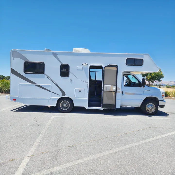 White RV rental/camper van parked on asphalt. Its side door is open under a clear blue sky, ready for your next adventure.. Thor Majestic 2019
