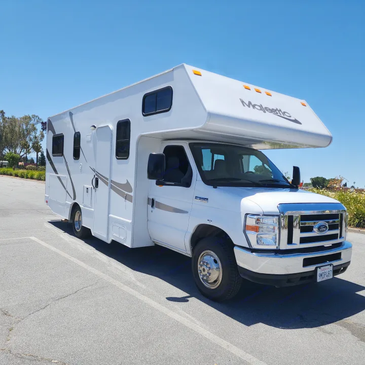 Bright white Majestic RV rental, a Ford E350 Super Duty, parked on asphalt under a sunny blue sky, ready for travel.. Thor Majestic 2019