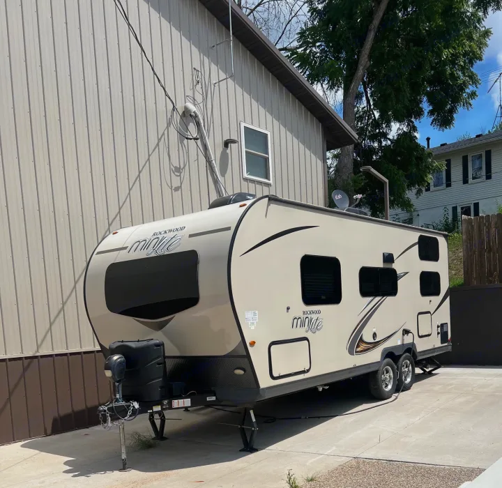 This beige Rockwood Mini Lite travel trailer, ideal for an RV rental, is perfectly parked on a sunny concrete area beside a building.. Forest River Rockwood Mini Lite 2020
