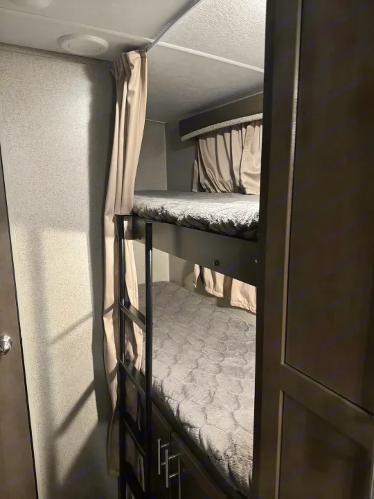This RV rental features two stacked bunk beds with grey blankets and privacy curtains, offering a cozy sleeping space.. Forest River Rockwood Mini Lite 2020