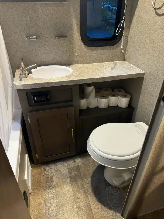 RV rental bathroom with a compact sink, toilet, and window. Organized storage for toilet paper. Ideal for your next road trip.. Forest River Rockwood Mini Lite 2020