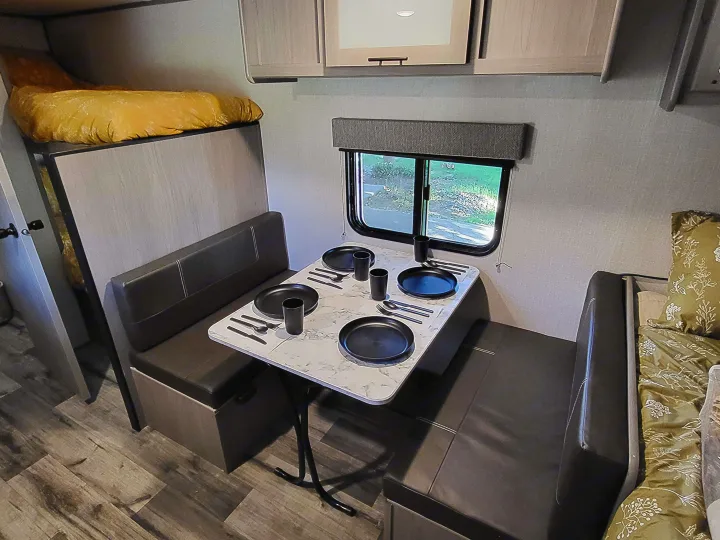 RV rental interior: A compact dinette set for four, with window views, overhead storage, and a cozy bunk bed.. Dutchmen Coleman Lantern LT 2023