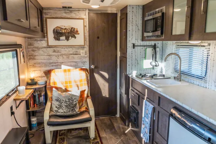Cozy RV rental interior: compact kitchen, rustic decor, and a comfy reading nook with a bear art piece. Ideal for travel.. Forest River Salem Cruise Lite 2018