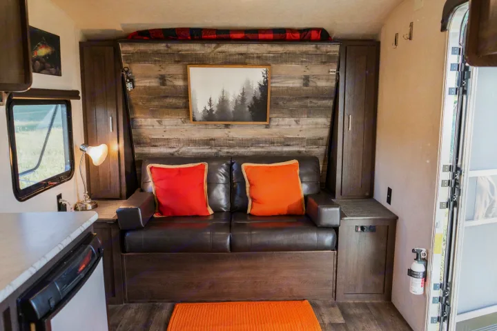 This RV rental offers a cozy living space with a dark leather couch, red/orange pillows, and rustic forest wall art.. Forest River Salem Cruise Lite 2018