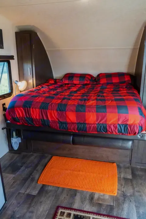 This RV rental features a cozy bedroom with red buffalo plaid bedding, wood floors, and built-in storage.. Forest River Salem Cruise Lite 2018