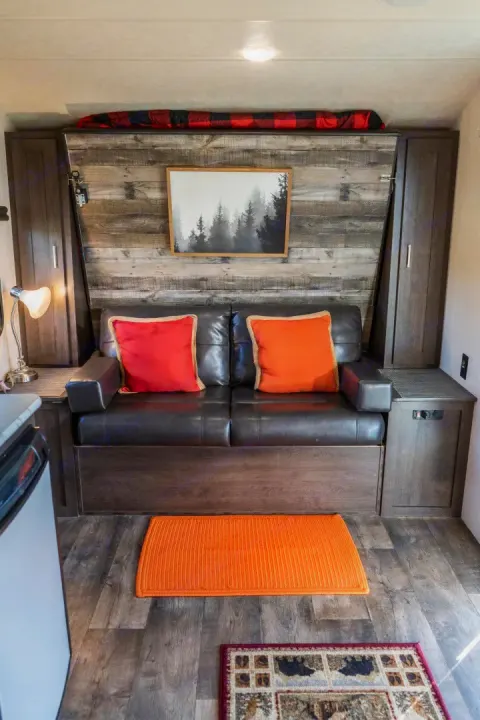 Cozy RV rental interior with a brown sofa, colorful pillows, and rustic wood-paneled wall. Perfect for road trips.. Forest River Salem Cruise Lite 2018