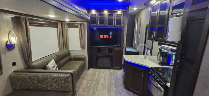 Spacious RV rental interior with cozy living area, Netflix TV, fireplace, and modern kitchen. Blue accent lighting creates a relaxing ambiance.. Forest River Cherokee Arctic Wolf 2018