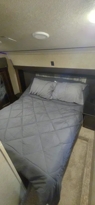 Inside an RV rental: a cozy bedroom with dark gray bed, integrated storage, and overhead vent.. Forest River Cherokee Arctic Wolf 2018