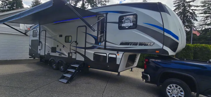 Large grey & blue Arctic Wolf fifth-wheel RV with extended awning, connected to a truck. Ideal for your next RV rental adventure.. Forest River Cherokee Arctic Wolf 2018