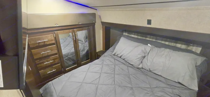 Cozy RV rental bedroom featuring a comfortable gray bed, built-in wardrobe with mirrored doors, and overhead lighting.. Forest River Cherokee Arctic Wolf 2018