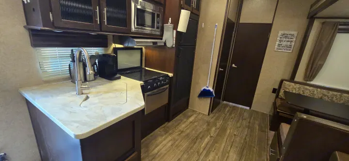An rv rental's well-equipped kitchen area with a sink, microwave, stove, and adjacent dinette.. Forest River Cherokee Arctic Wolf 2018