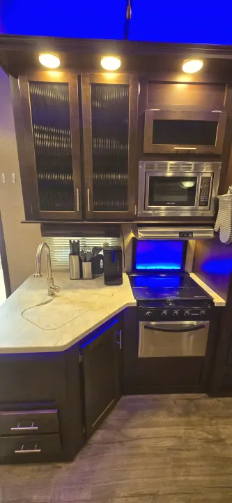 Bright RV rental kitchen with dark cabinets, modern appliances, a sink, and cool blue accent lighting.. Forest River Cherokee Arctic Wolf 2018