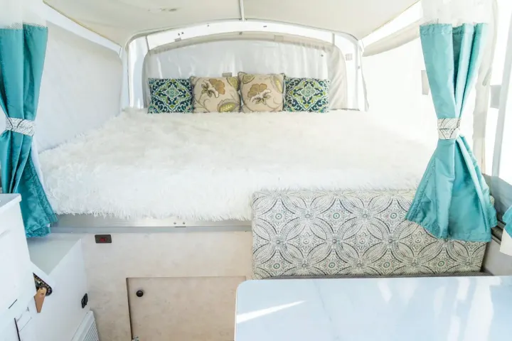 Stylish RV rental interior featuring a comfy bed with fluffy blanket, patterned pillows, and teal curtains.. Coleman Grand Tour Sun Ridge 1998